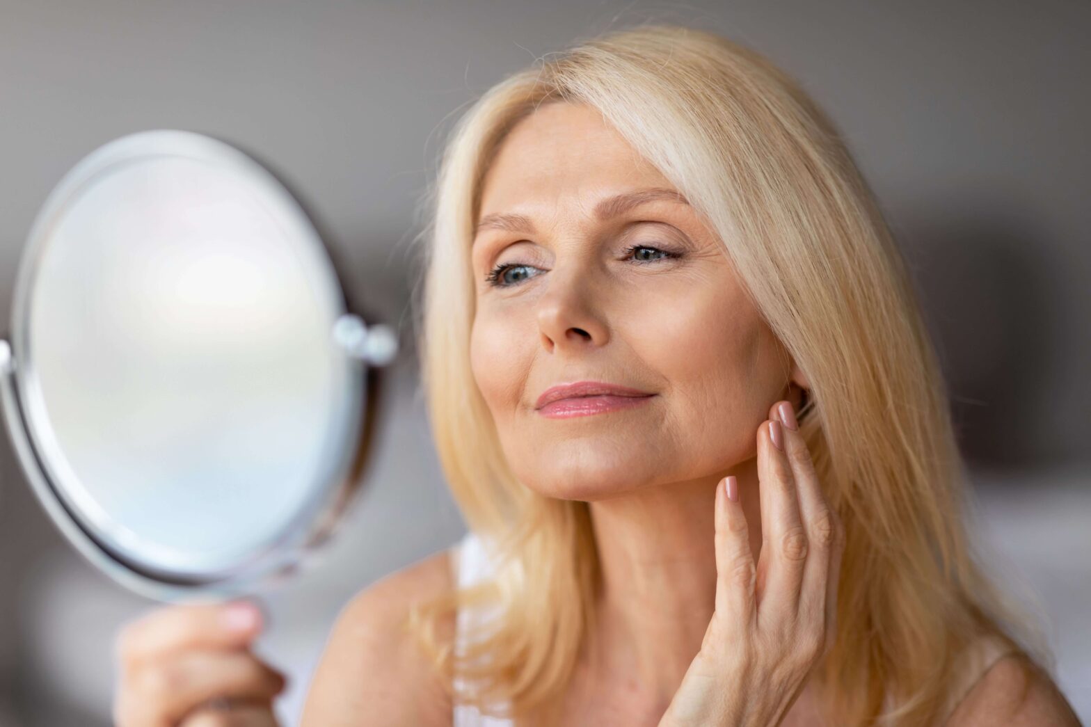 older woman, looking in mirror, touching face